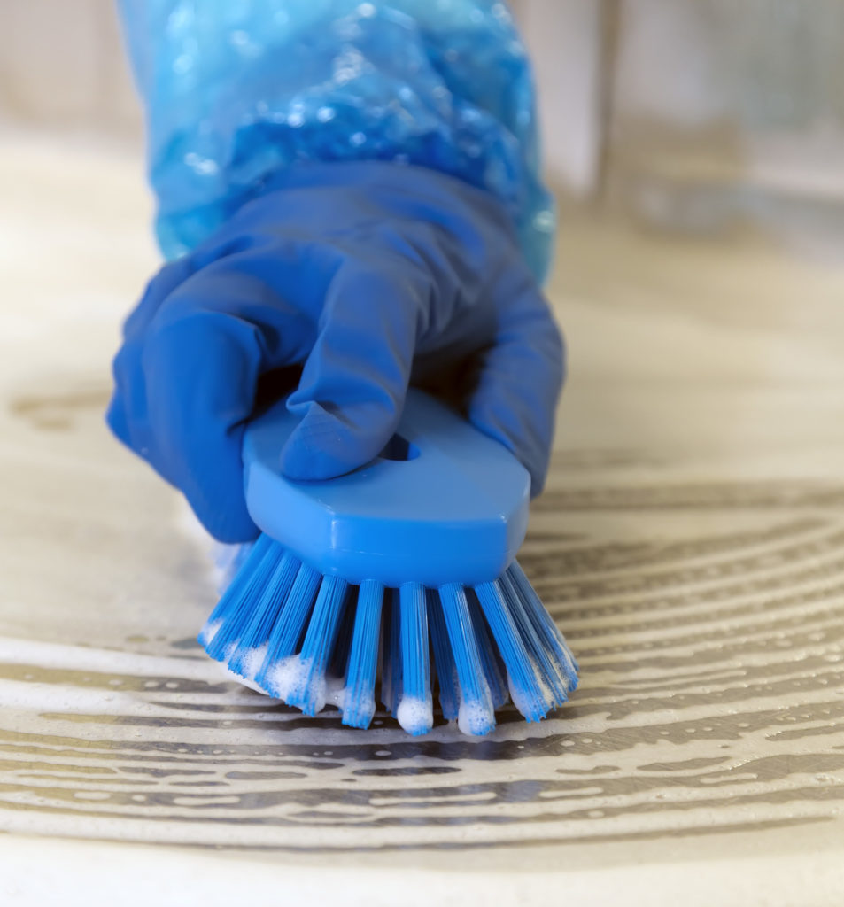 Gloved hand scrubbing table with blue scrub brush